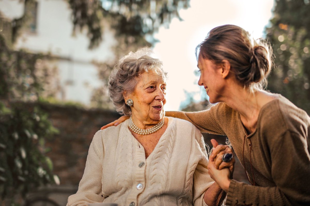 Woman holding an older woman’s hand while chatting in a garden